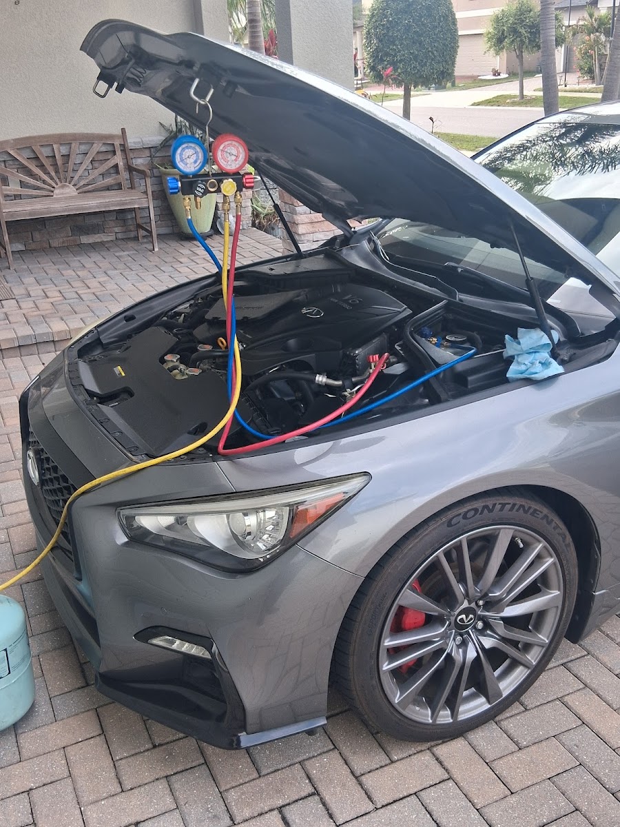 Mechanic servicing AC system on a silver Infiniti Q50 outdoors